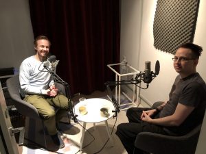 Två män sitter i podcaststudion vid varsin mikrofon